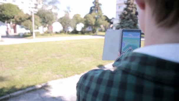 Jonge hipster man met behulp van de tablet in het stadspark spelen pokemon gaan. — Stockvideo