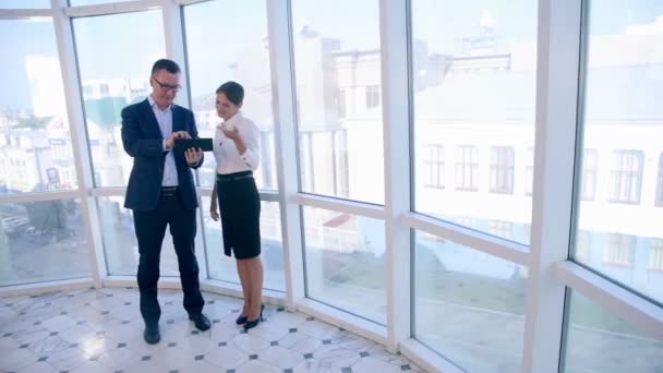 Negocios, arquitectura y concepto de oficina. Dos empresarios exitosos discuten proyecto en tableta en oficina brillante limpia cerca de ventana panorámica . — Vídeo de stock