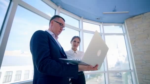 Biznesmeni mężczyzna i kobieta omawiają projekt pracy w nowoczesnym budynku biurowym w pobliżu czystego okna panoramicznego. Koncepcja biznesowa. Strzelać Steadicam. — Wideo stockowe