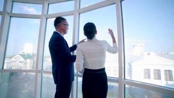 Empresarios hombre y mujer discuten proyecto de trabajo en un moderno edificio de oficinas cerca de una ventana panorámica limpia. Concepto de negocio. Steadicam disparar . — Vídeos de Stock