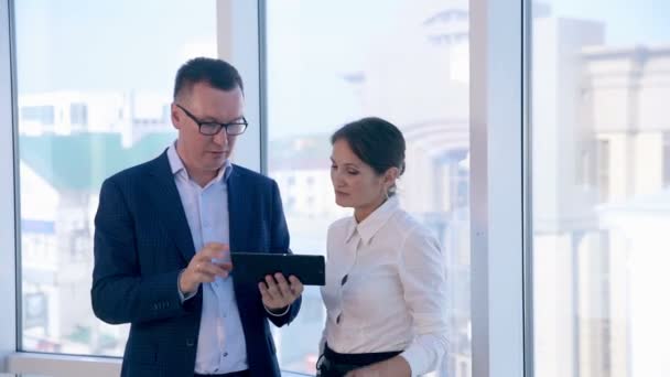 Los colegas discuten el proyecto en la tableta en la oficina limpia brillante cerca de la ventana panorámica. Negocios, concepto de trabajo en equipo . — Vídeos de Stock