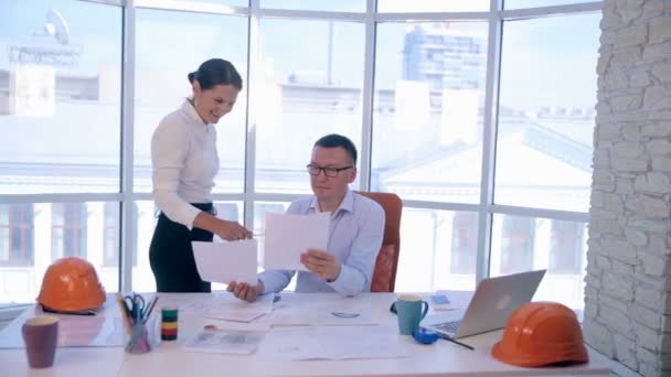 Een zakenman en zakenvrouw, ingenieurs helder schoon office. Bespreking van de het bouwproject, een plan, een tekening, een regeling. — Stockvideo