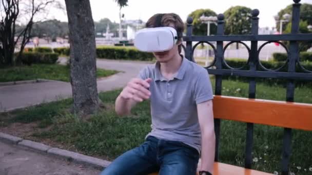 仮想現実を身に着けている若いハンサムな男は、都市公園におけるゴーグルします。. — ストック動画