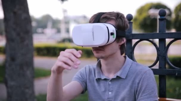 Young handsome man wearing virtual reality goggles in a city park. — Stock Video