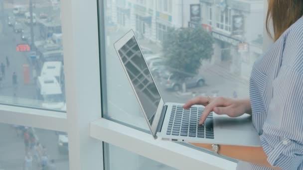Жінка використовує ноутбук біля панорамного вікна в сучасному яскравому офісі . — стокове відео
