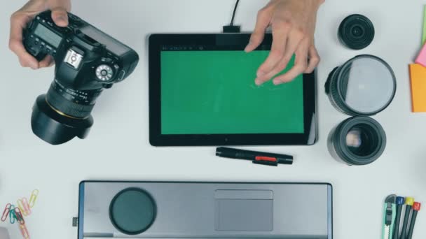 Workplace from above. Unrecognizable photographer working with his camera, tablet, memory card. Top view, greenscreen on tablet. — Stock Video