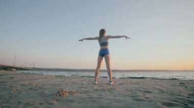 İnce bir rakam olan kadın jimnastik güneş doğarken devreye girer. Ağır çekim. 100 fps.