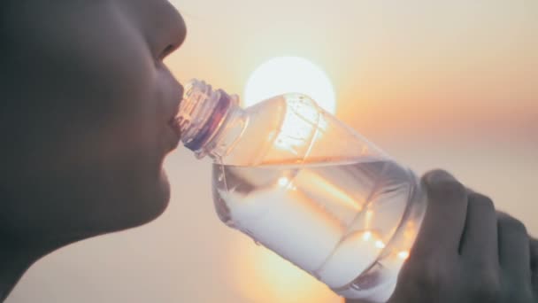 Young Athlete girl drinking water after fitness run, jogger training at summer sunset. Slow motion. Close up. — Stock Video