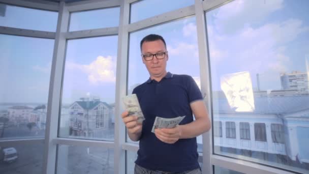 Un uomo che conta dollari alla luminosa finestra panoramica. Risparmio di denaro, economia, concetto di cassa . — Video Stock