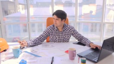 Young busy businessman working with drawings, blueprints in a light, modern office.