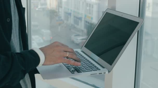 Onherkenbaar man aan het werk op laptop in de buurt van panoramisch venster in moderne kantoor. Stadsgezicht op de achtergrond. — Stockvideo