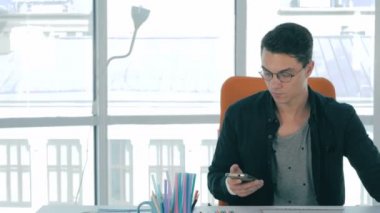 Yakışıklı tasarımcı yaratıcı ofisinde oturan ve smartphone kullanarak.