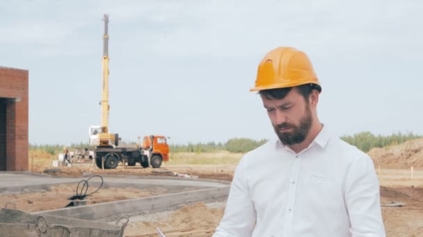 Homme barbu patron de construction vêtu d'un chapeau dur contrôle le processus de construction . — Video