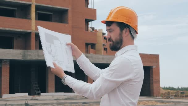 Arquitecto jefe en la obra. Arquitecto jefe en un casco en el sitio de construcción mirando el plan, plano . — Vídeo de stock