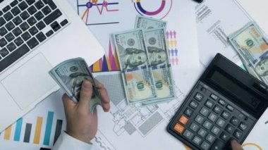 Başarılı erkekte sayım banknot para bize dolar hesap makinesi üzerinde uygun. Görünümünün üzerinde. Grafikler, dizüstü bilgisayar, hesap makinesi bir tablo.