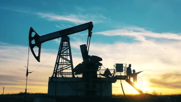 Deux travailleurs des champs pétrolifères estimant le pétrole en place au coucher du soleil — Video