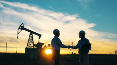 İki mühendis gün batımında petrol pompasının önünde el sıkışıyor.