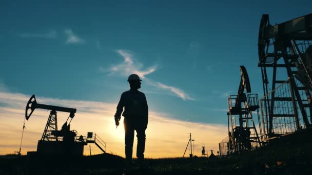 Silhouet van oliearbeider omringd door oliepompen op olieveld — Stockvideo