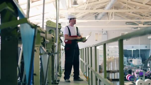 Работник завода контролирует процесс производства с помощью ноутбука — стоковое видео