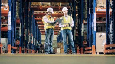 Depoda dizüstü bilgisayarı olan erkek mühendisler konuşuyor.