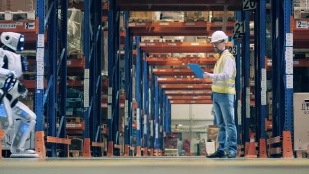 Lagerarbetare inventerar lådor som drivs av en människoliknande robot — Stockvideo