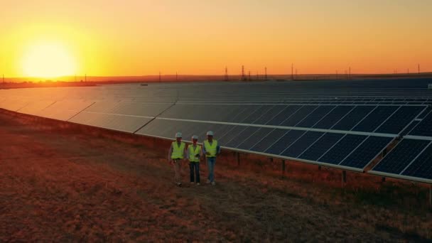 Uitzoomen vanuit de lucht van werknemers die bij zonsondergang over zonneparken lopen — Stockvideo