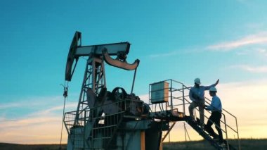Erkek mühendisler bir pompa sopasının üzerinde durup bölgeyi izliyorlar. Fosil yakıt, ham petrol konsepti.
