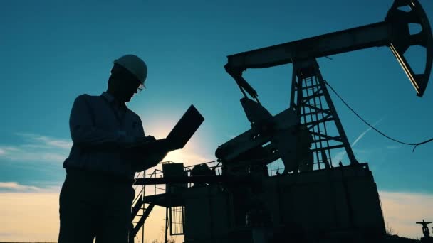 Hombre trabajador está haciendo cálculos en el sitio de bombeo de petróleo. Combustible fósil, concepto de petróleo crudo. — Vídeos de Stock