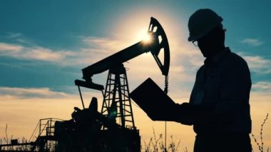 Erkek mühendis ve güneş ışığında çalışan bir pompa. Petrol ve gaz endüstrisi kavramı.
