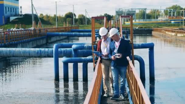 Twee ingenieurs passeren de buitenvoorzieningen voor afvalwater. Concept afvalwaterzuivering. — Stockvideo