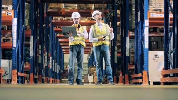 Dos trabajadores de almacén hablando, carretilla elevadora moviéndose en el fondo — Vídeos de Stock