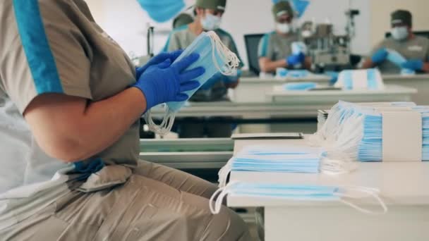 Varios trabajadores de la fábrica estirando y empacando máscaras faciales en una instalación de fabricación de máscaras médicas — Vídeo de stock