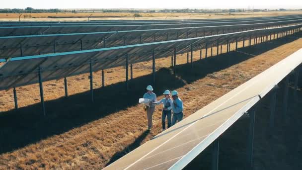 Drone shot van drie zonne-energie ingenieurs lopen in een zonne-park — Stockvideo