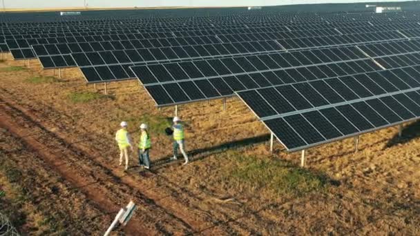 Drei Solarmodul-Techniker untersuchen einen Solarpark von oben — Stockvideo