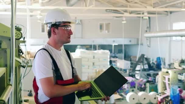 Fabrieksarbeider die zijn laptop gebruikt om het productieproces van plastic zakken te controleren — Stockvideo