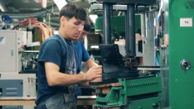 Erkek işçi, bitmemiş bir çizmeyi presin altına koyuyor.