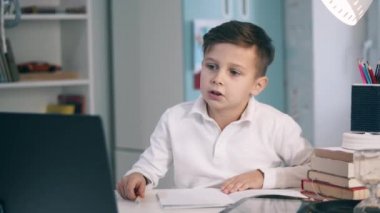 Odaklanmış küçük bir çocuk çevrimiçi bir ders sırasında not alıyor.