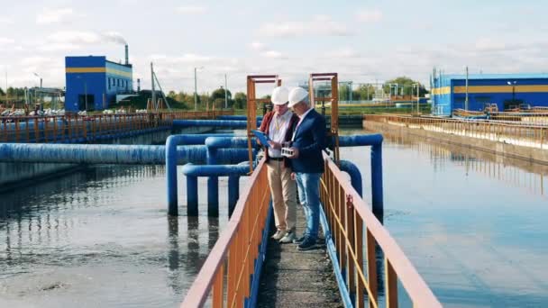 Sito di trattamento delle acque reflue con due ingegneri che discutono piani — Video Stock