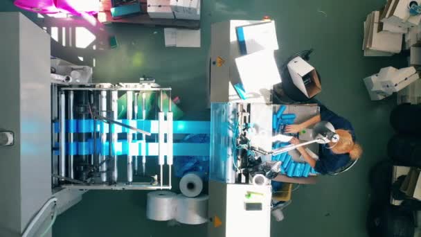 Vrouwelijke werknemer die blauwe plastic zakken uit een productielijn in een doos verpakt — Stockvideo