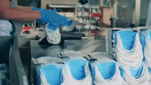 Batches of medical masks are getting put onto the belt by a worker — Stock Video