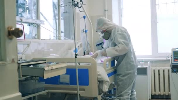 Trabajador sanitario que atiende a un paciente con coronavirus en una cama de cuidados intensivos — Vídeo de stock