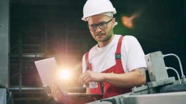 Bilgisayarlı bir mühendis fabrika ekipmanlarını inceliyor.