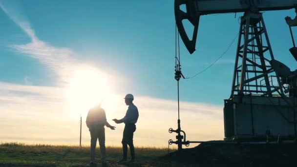 Petrol işçileri güneş ışığında bir petrol sahasını izliyorlar. — Stok video