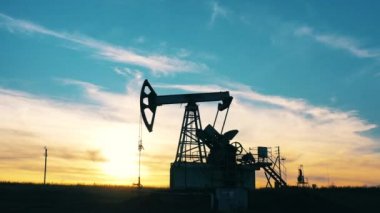 Gün batımında petrol sahasında çalışan bir yağ tulumbasının silueti