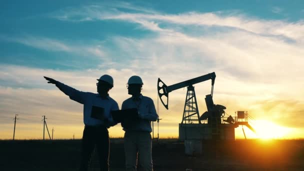 日落时分，石油工业工人在油田边与油泵交谈 — 图库视频影像