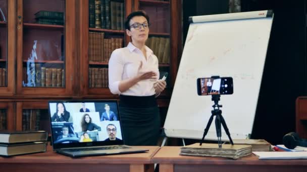 Professora está realizando uma aula online em uma biblioteca — Vídeo de Stock