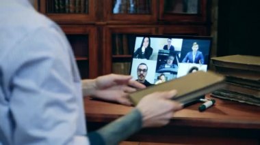 Bir adam ders sırasında online öğrencilere eski bir kitap gösteriyor.