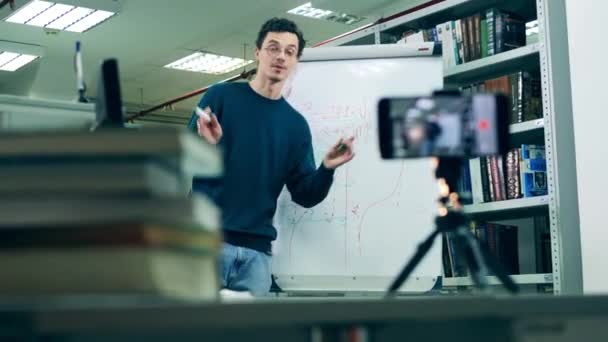 En man undervisar en online-lektion medan han är i ett bibliotek — Stockvideo