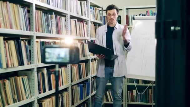 Un joven profesor imparte una clase de internet en una biblioteca — Vídeo de stock