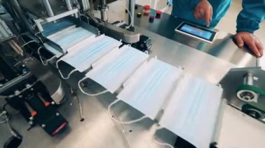 Bir tıbbi maske fabrikasında yüz maskesi üretim hattını kontrol eden fabrika işçisi.